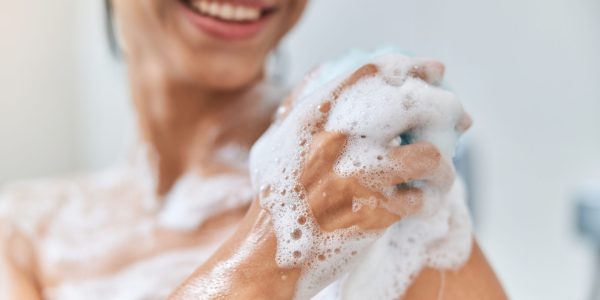 Close up of smiling lady with foamy washcloth in her hand taking shower at home