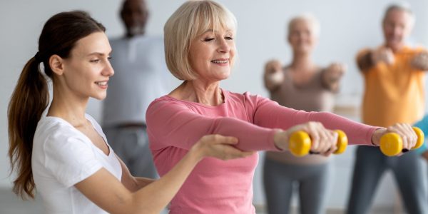 Young,Lady,Coach,Helping,Senior,Woman,While,Exercising,With,Dumbbells,