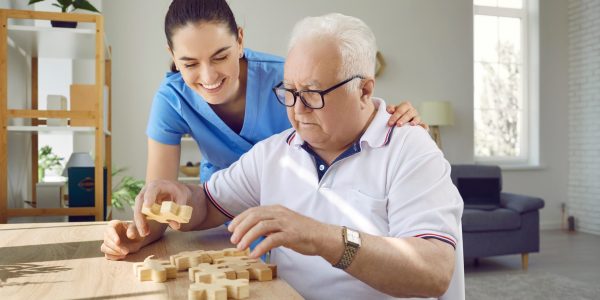 Nurse,In,Retirement,Home,Helping,Old,Male,Patient,With,Board