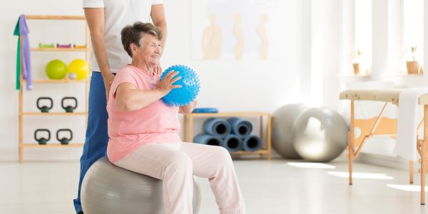 Happy,Senior,Woman,Sitting,On,Grey,Ball,And,Holding,Blue